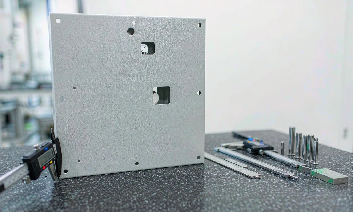 Quality engineer measuring a metal enclosure panel with a digital caliper